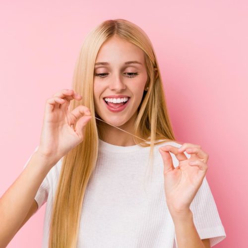 Young blonde woman cleaning her teeth with a floss